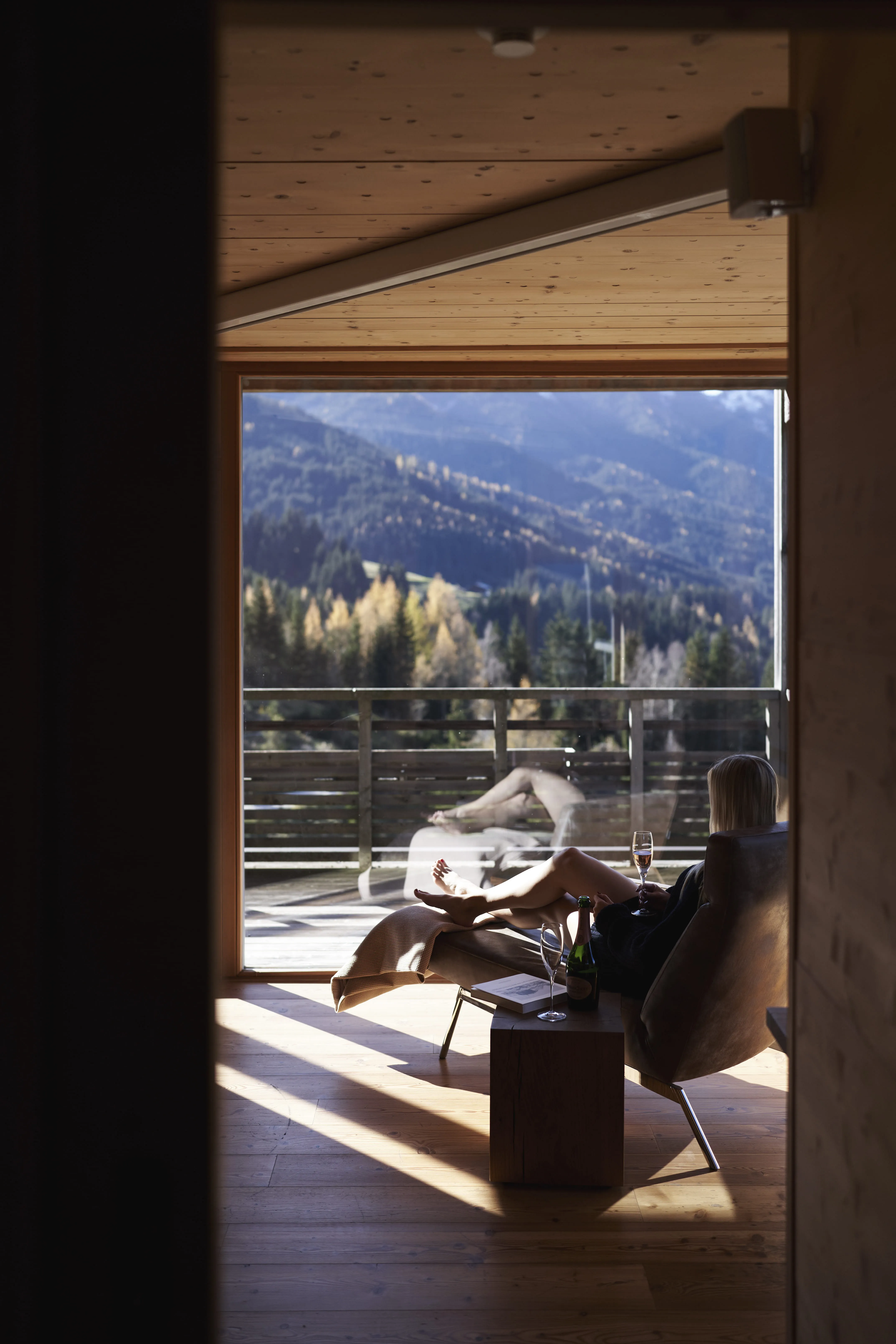 Person entspannt auf der Veranda im Holzhotel Forsthofalm mit Blick auf die Berge