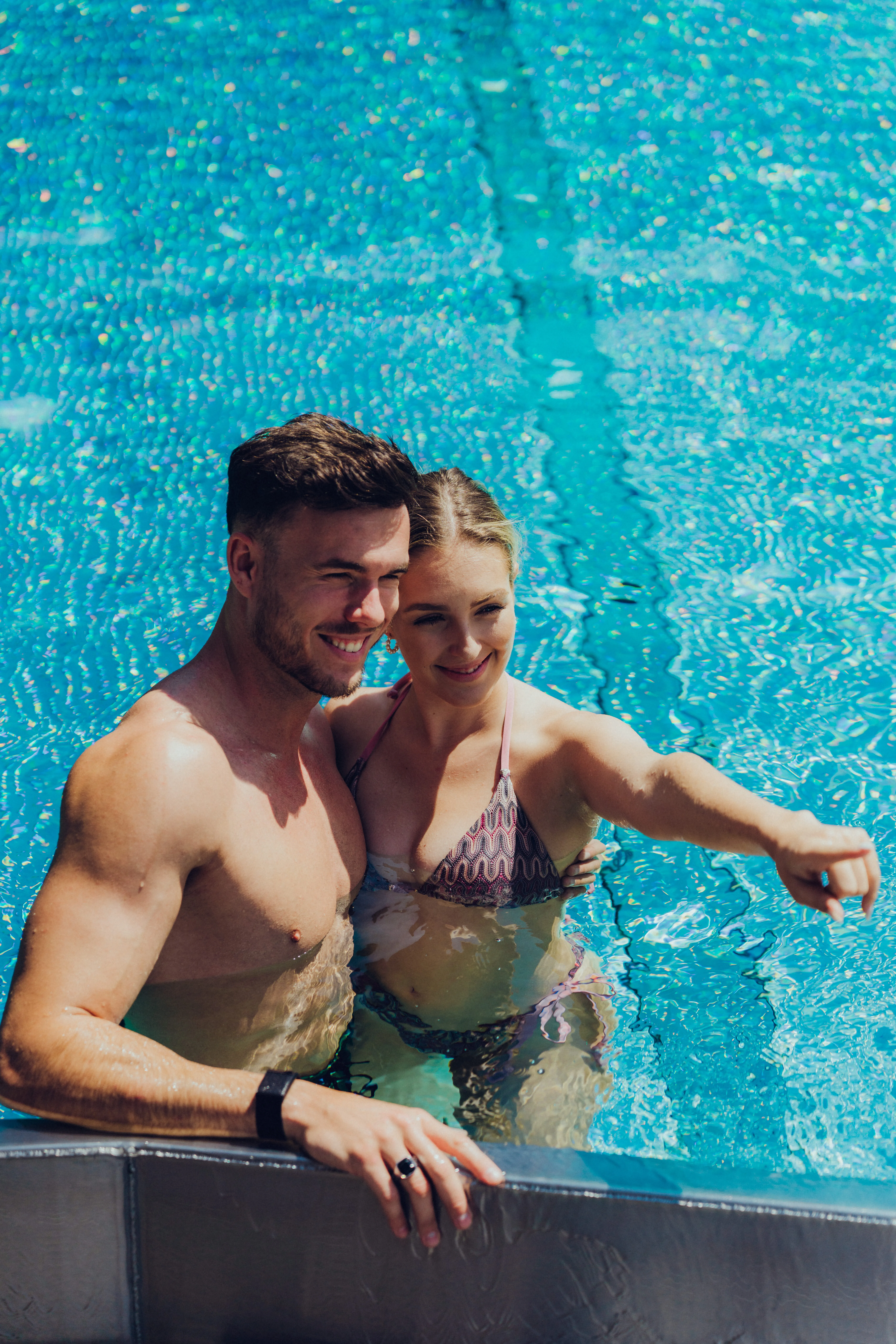 Paar posiert lächelnd am Rande eines Schwimmbeckens