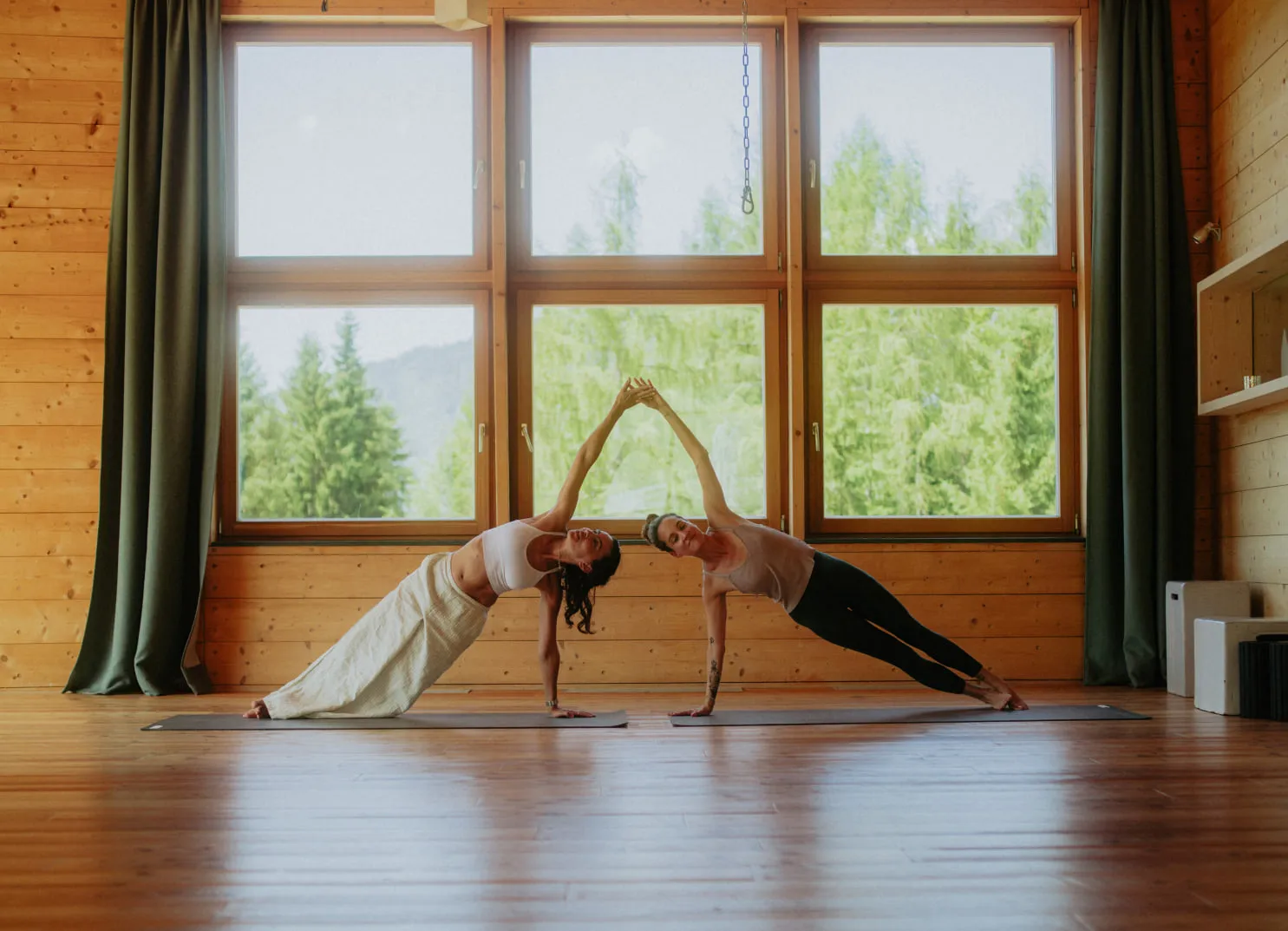 Zwei Personen in Yoga-Posen in einem Holzraum