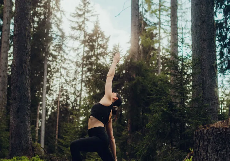 Frau macht Yoga zwischen hohen Bäumen im Wald