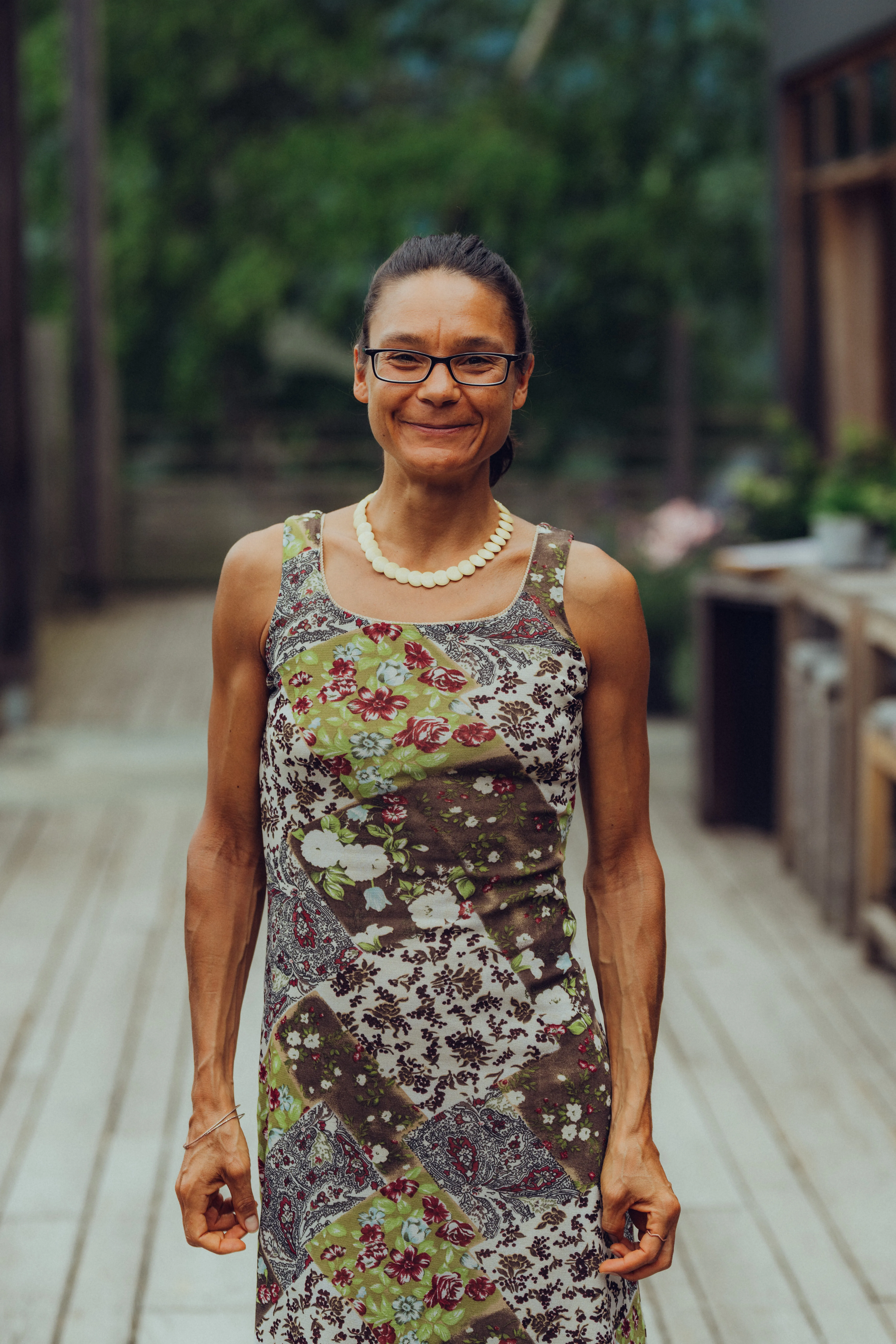 Person in einem Blumenkleid und Brille, lächelt im Freien