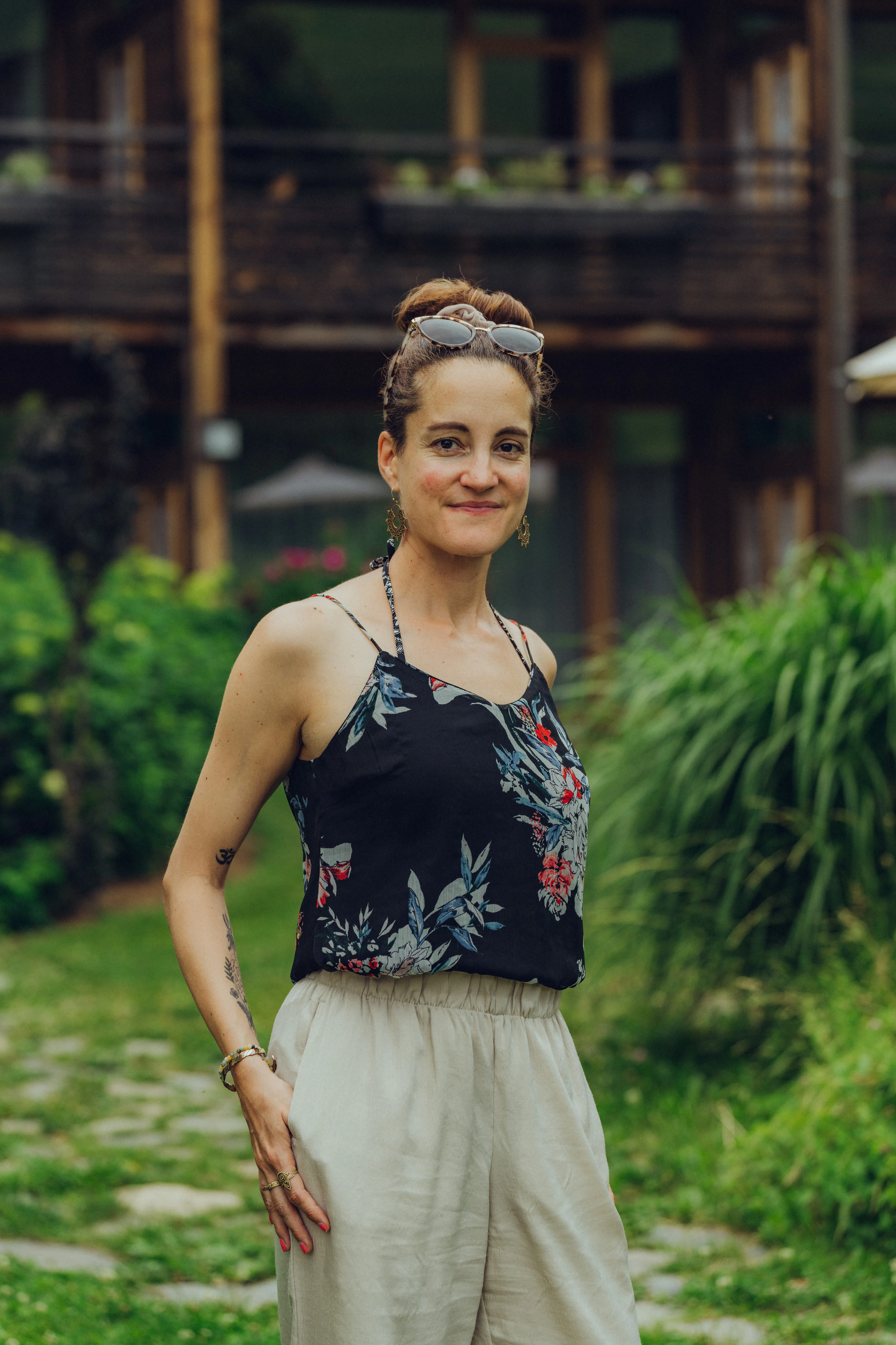 Frau in floralem Oberteil und hellen Hosen im Freien.